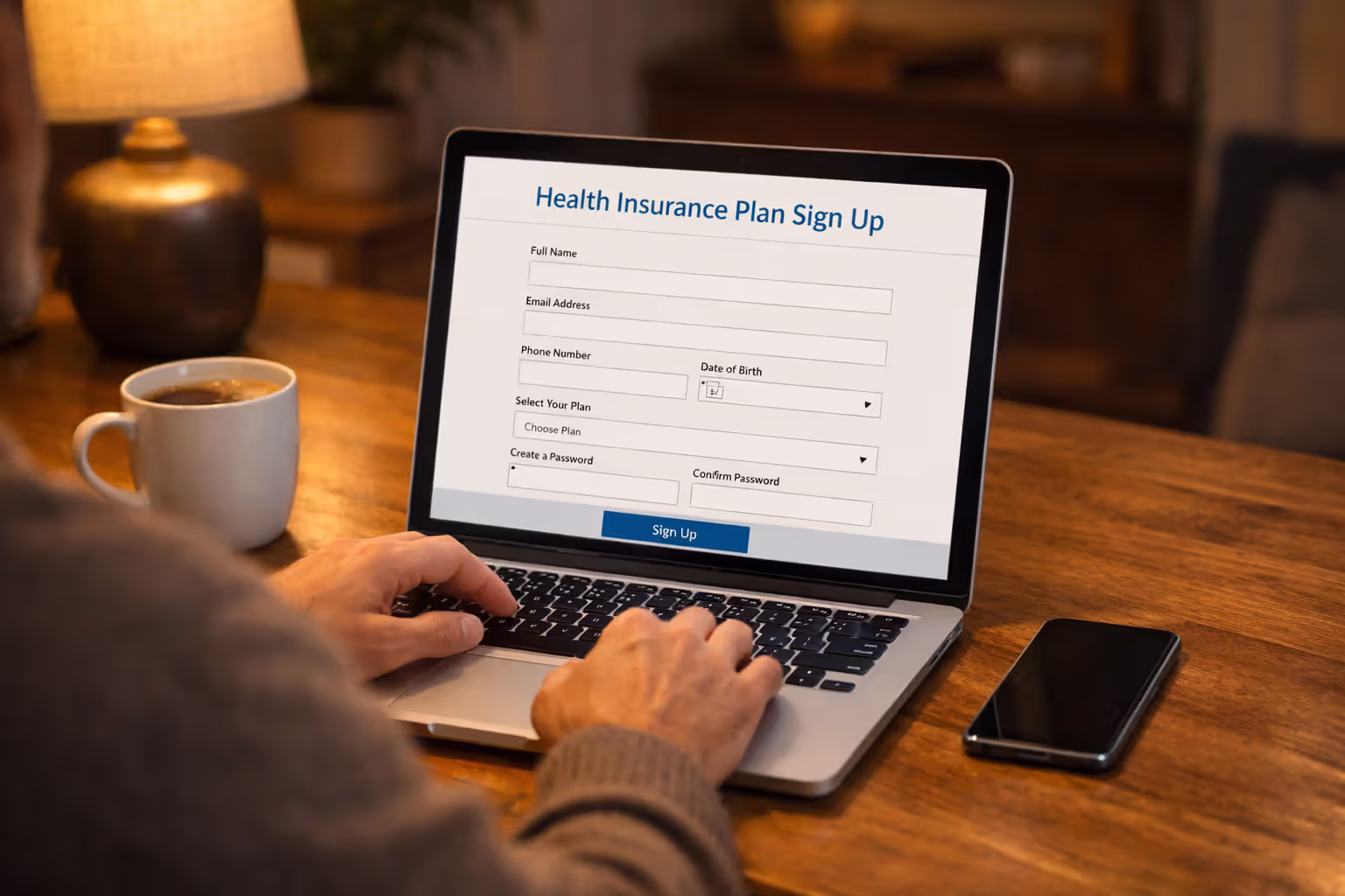 Person enrolling in a dental insurance plan online using a laptop at a home desk with coffee cup nearby