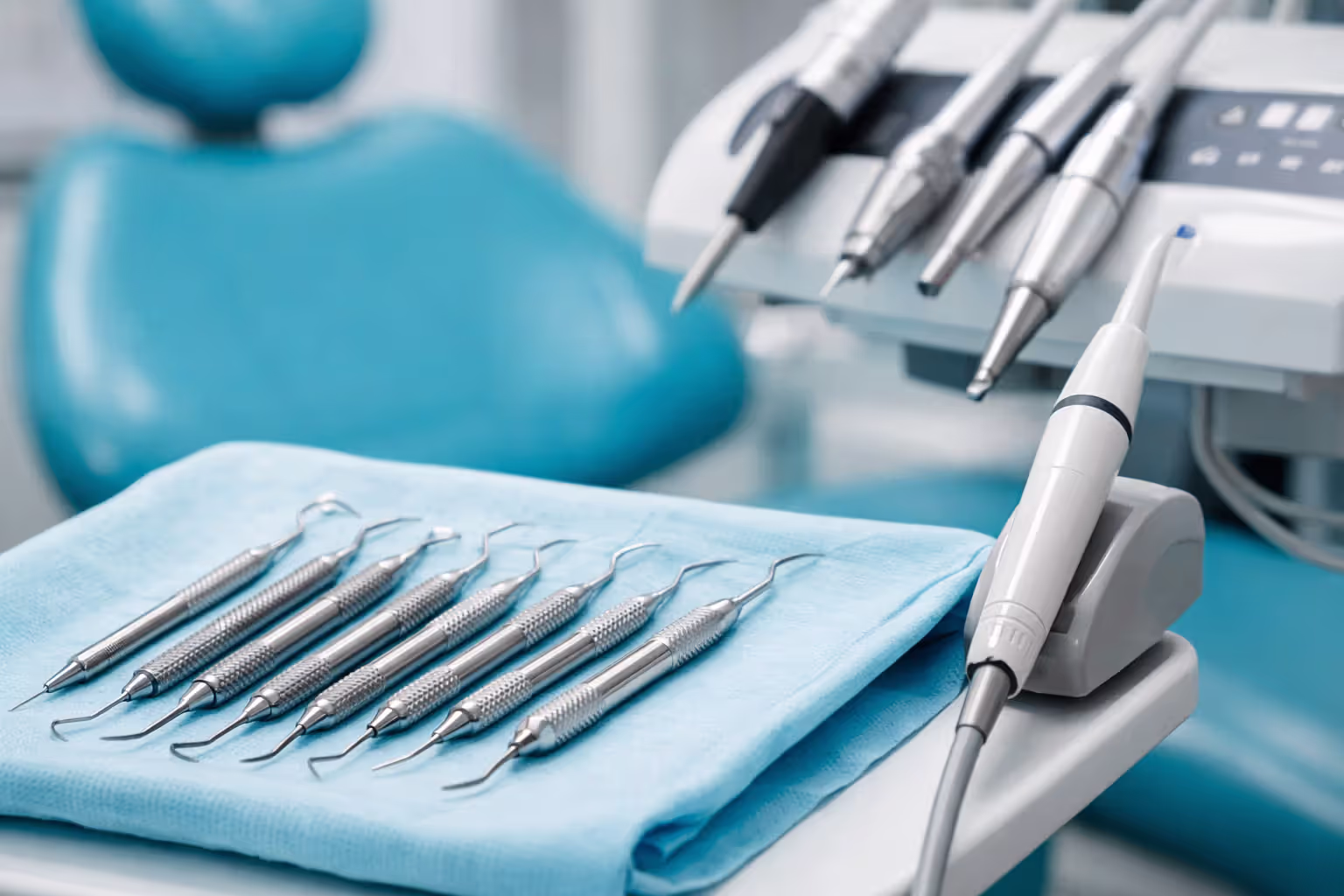 Dental scaling instruments including ultrasonic scaler and curettes arranged on sterile tray with dental chair in background