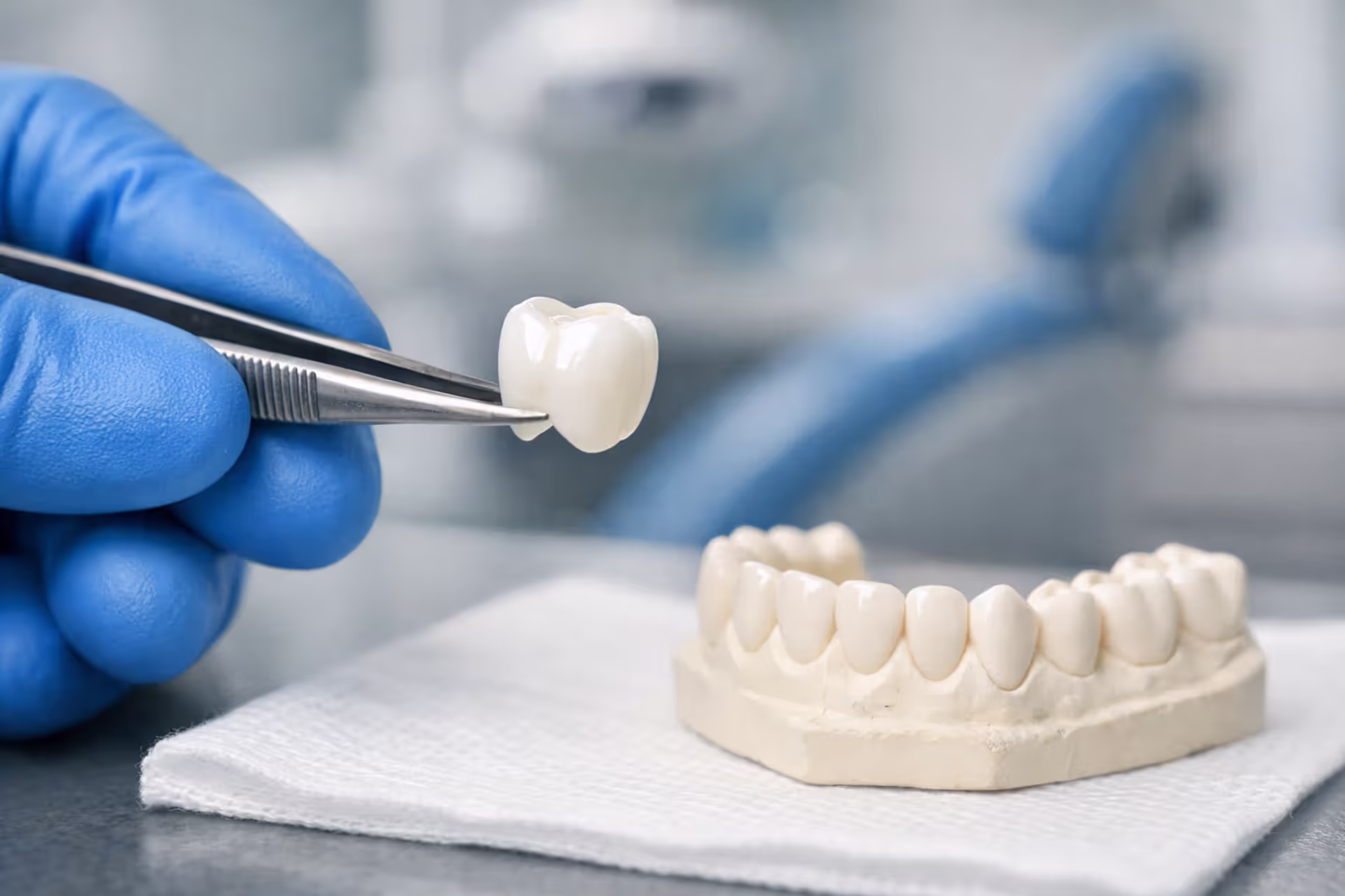A dentist in blue gloves holding a white ceramic dental crown with dental tools and a tooth impression on a sterile tray in a modern dental office