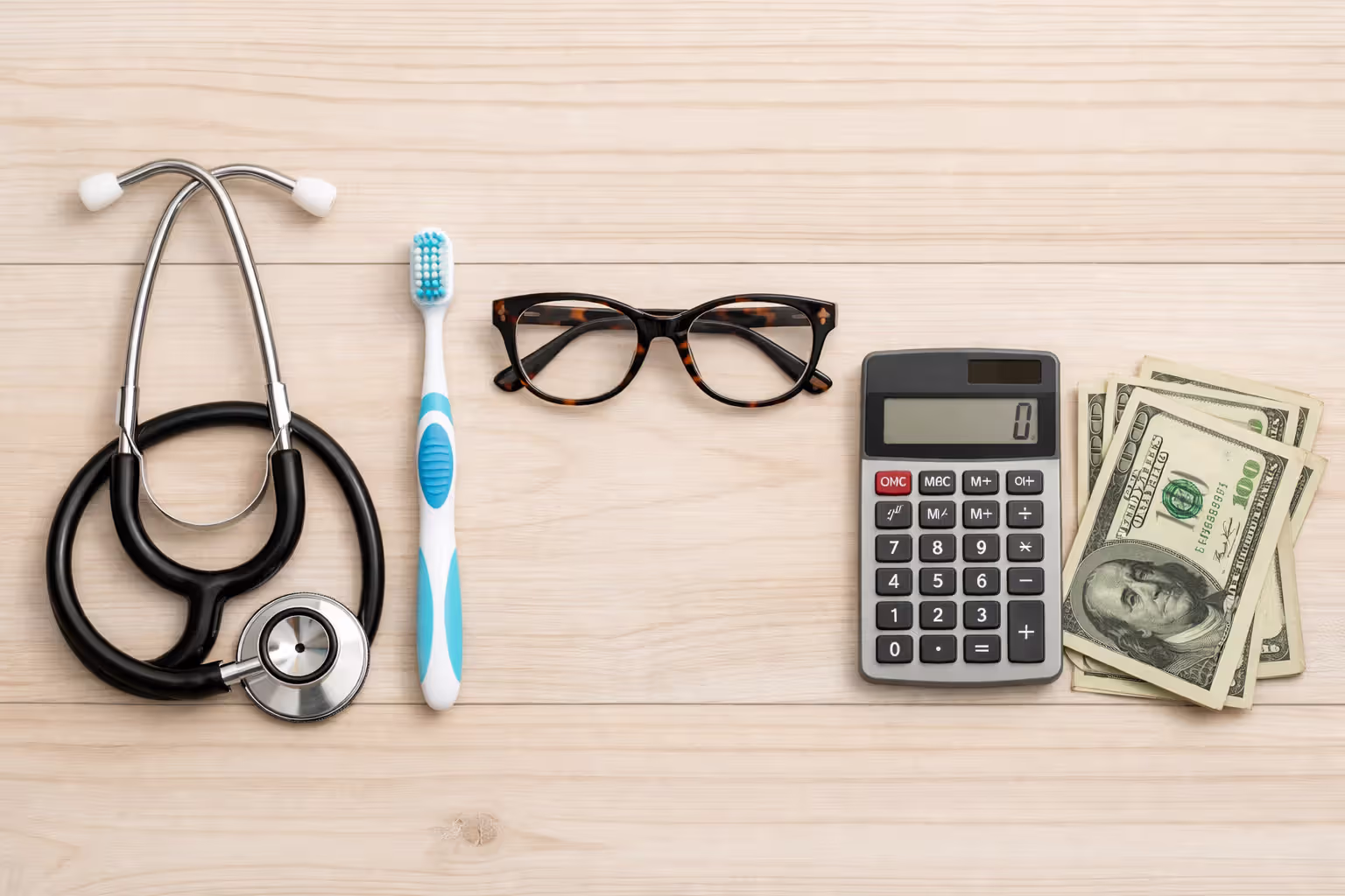 Flat lay of stethoscope, toothbrush, eyeglasses, calculator, and dollar bills representing dental and vision insurance costs
